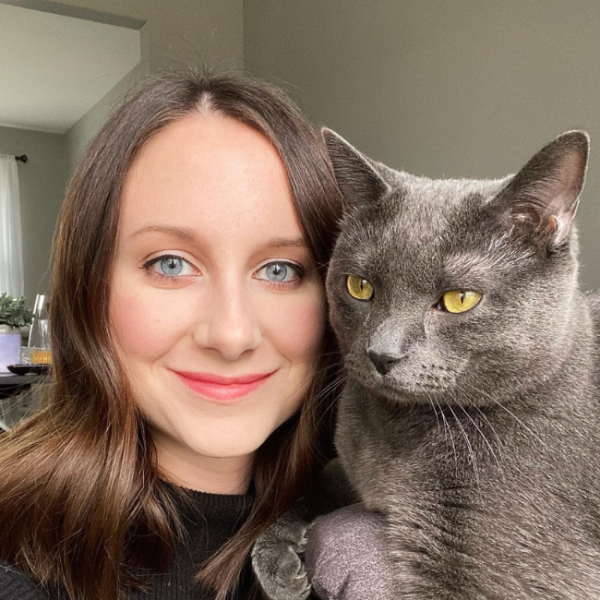 Woman with blue eyes holding a gray cat with yellow eyes.