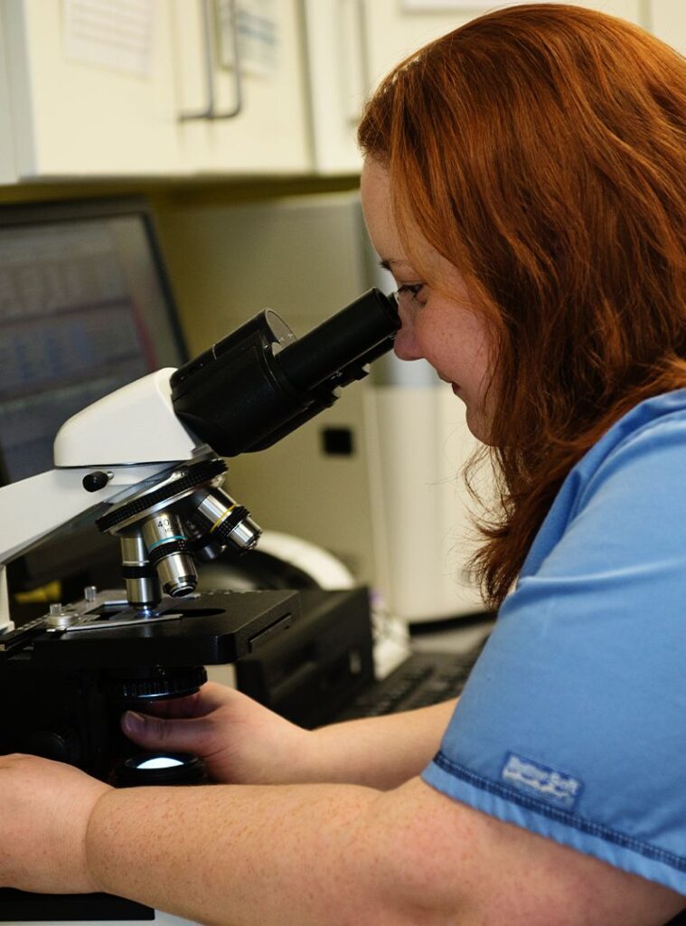 Woman with red hair using a microscope in a lab setting.