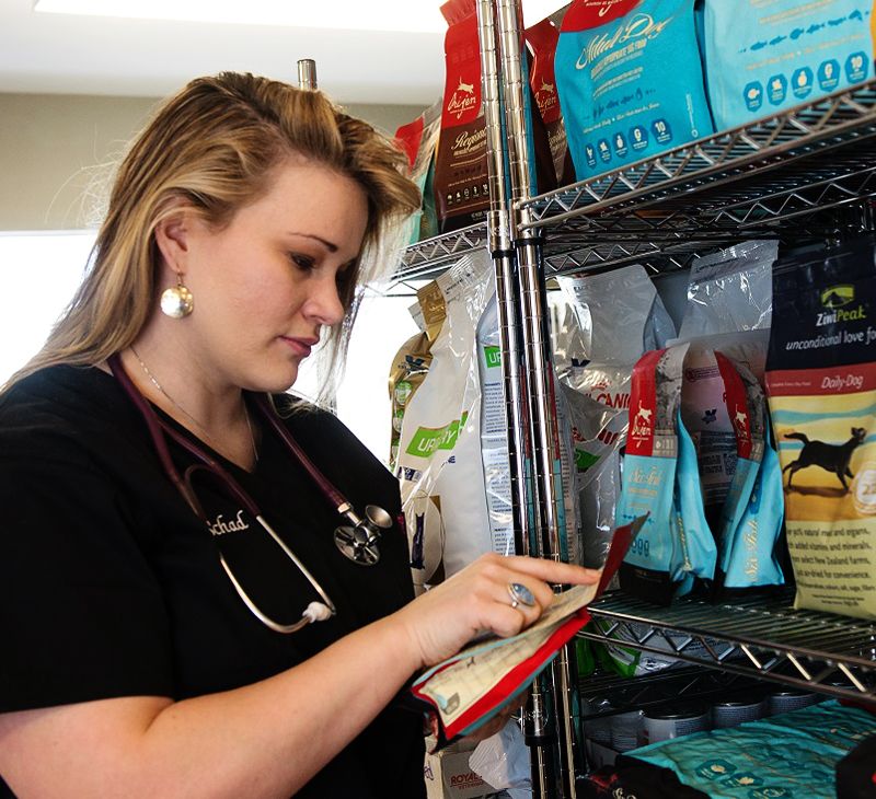 A veterinarian in scrubs examines a product in a pet supply shelf.