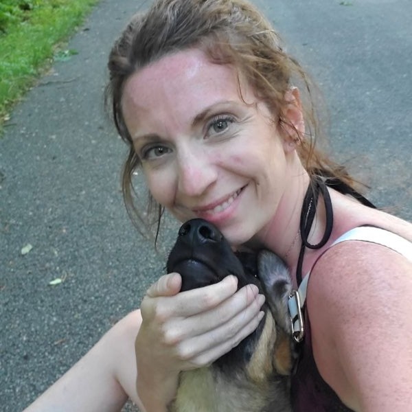 Woman smiling while hugging a black and tan dog outdoors.