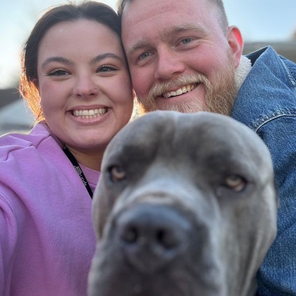 Smiling couple with a gray dog in the foreground.