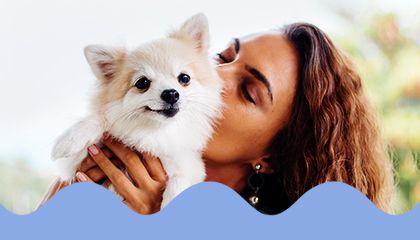 Woman kissing a fluffy Pomeranian puppy she is holding.